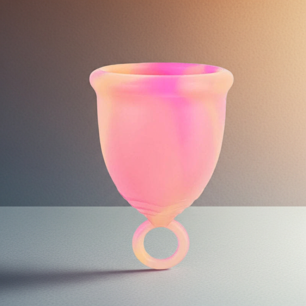 Pink and orange menstrual cup on a neutral background with eucalyptus leaves.