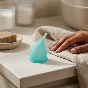 Turquoise cup on a bathroom counter with a hand and towel in the background